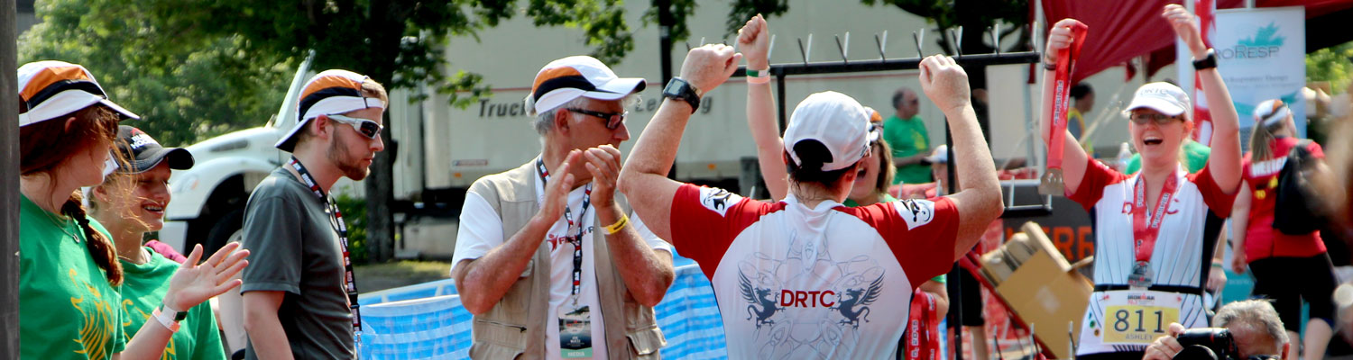 person crossing the finish line of an ironman with their hands in the air wearing a DRTC tri suit