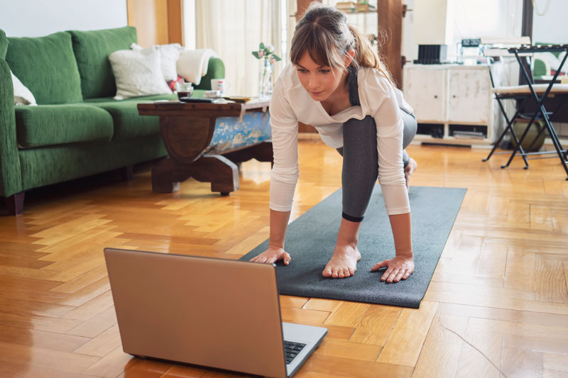 woman doing yoga at home watching her laptop