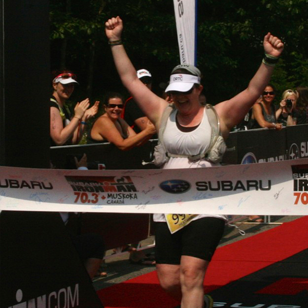 Heather Bowie crossing a finish line with her arms raised in victory